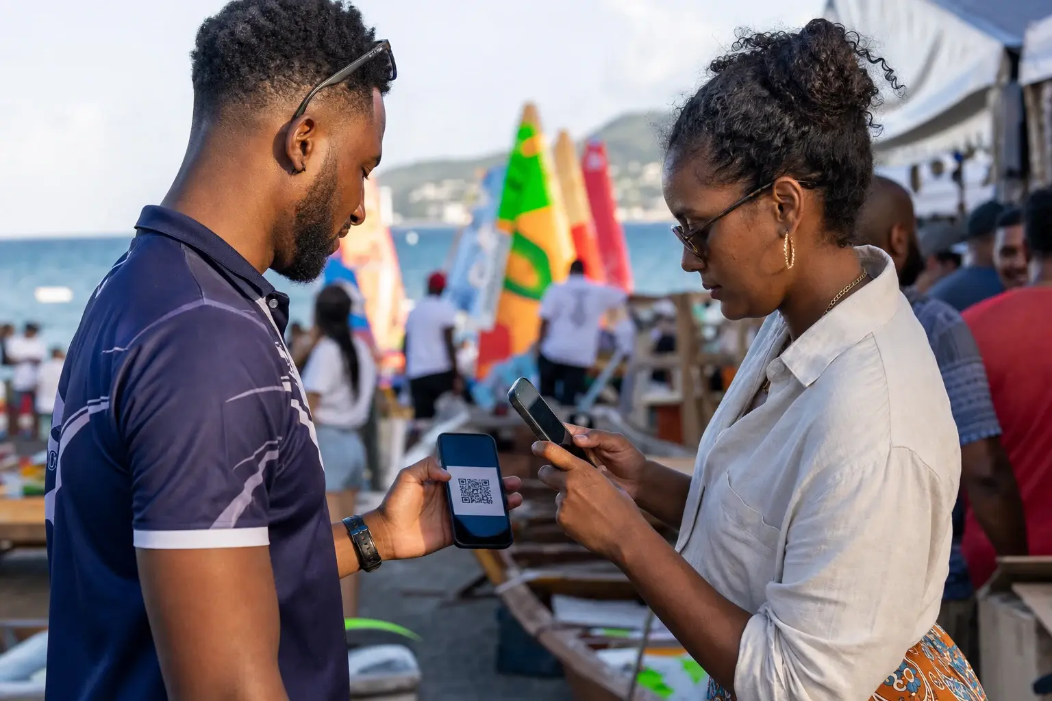 Sur la plage, devant des voiles colorées, deux personnes échangent leur Hub par QR code.